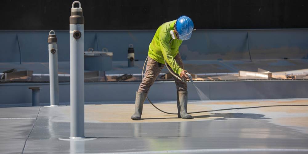 worker using an industrial spray gun to apply a coating to a commercial roof