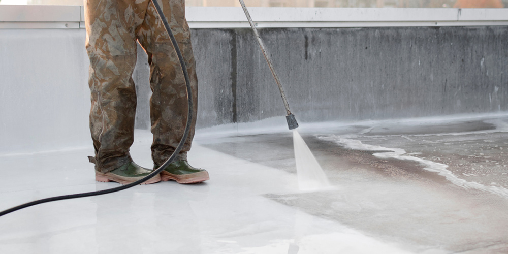 person with rubber boots water blasting a roof to clean it